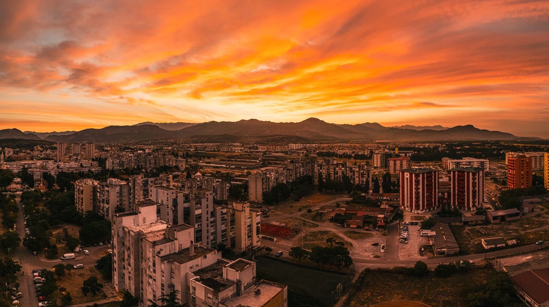 Stunning aerial view of Podgorica cityscape at sunset, featuring vibrant orange skies and architecture.