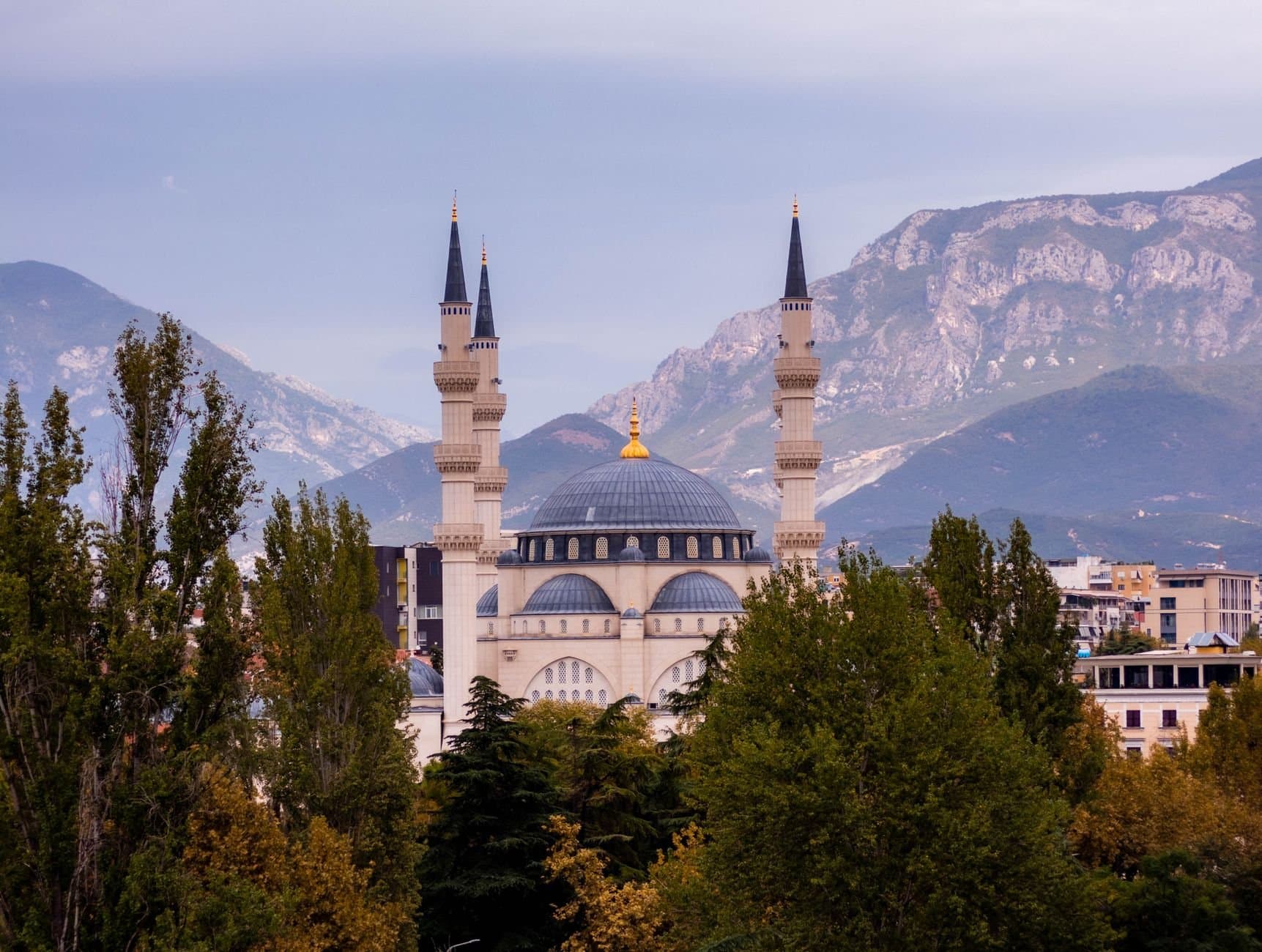 View of Namazgah Mosque in Tirana, Albania, framed by mountains and trees, showcasing stunning Islamic architecture.