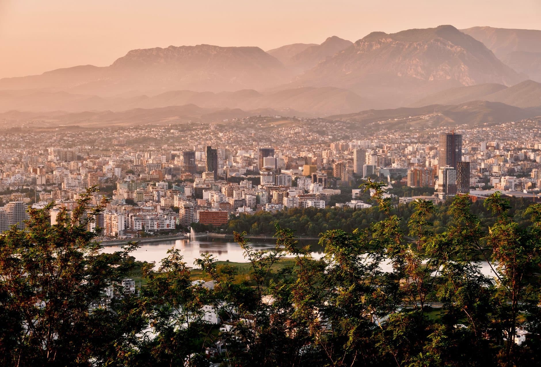 A stunning aerial view of Tirana's skyline framed by mountains and lush greenery during sunset.
