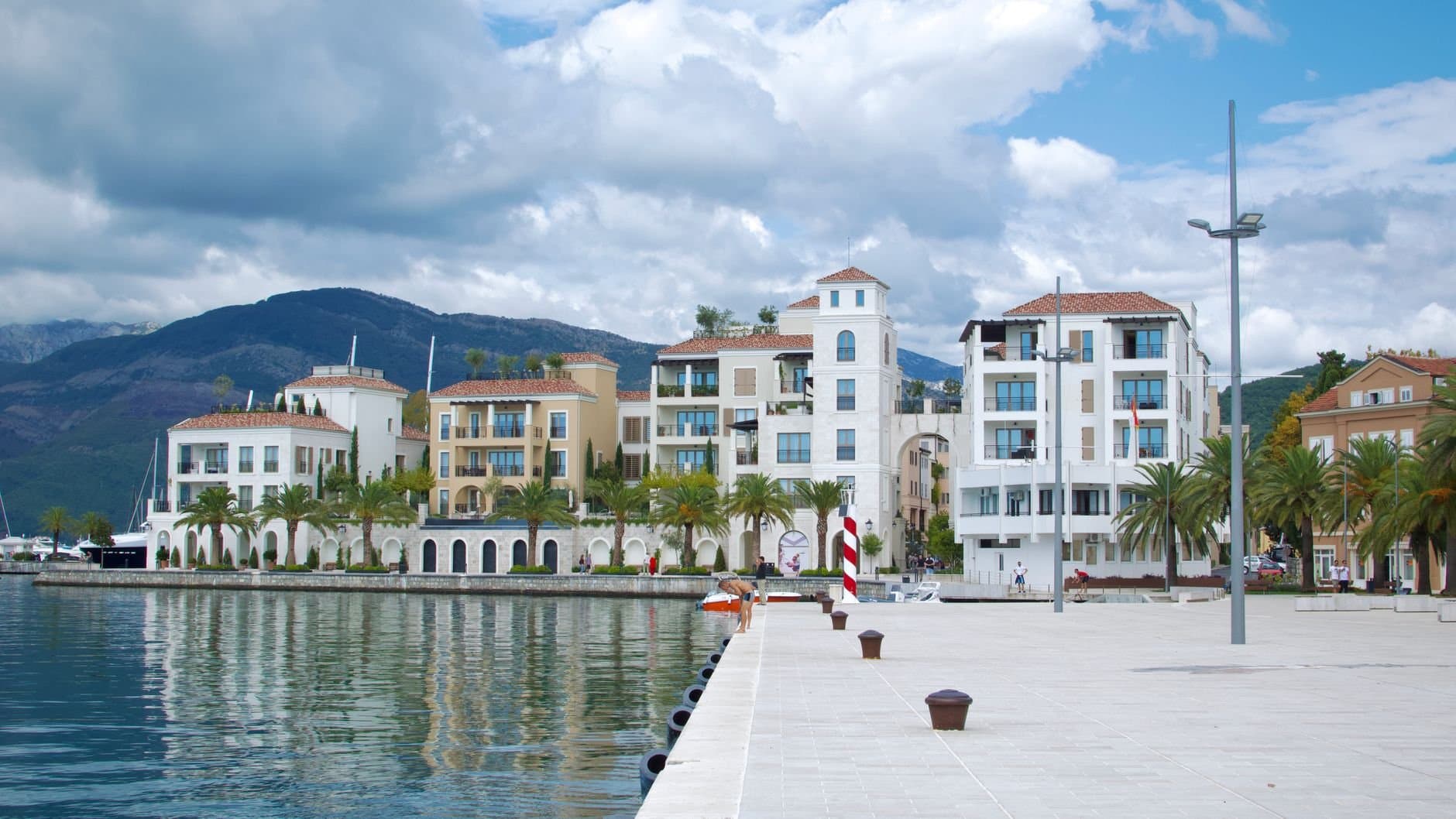 Beautiful waterfront buildings in Tivat, Montenegro, with mountains and a cloudy sky.