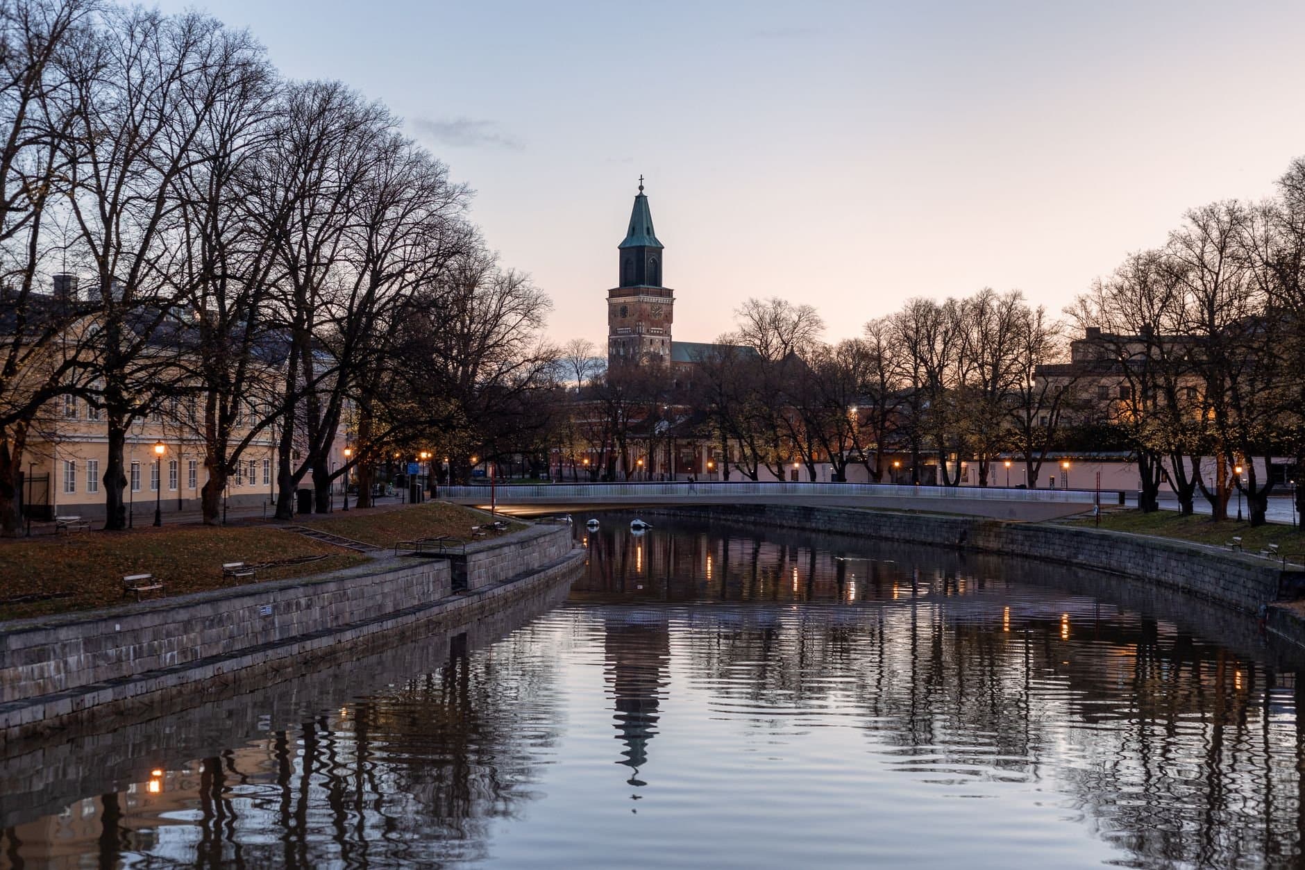 Turku Cathedral with bare trees reflecting on the river in Finland at dusk.