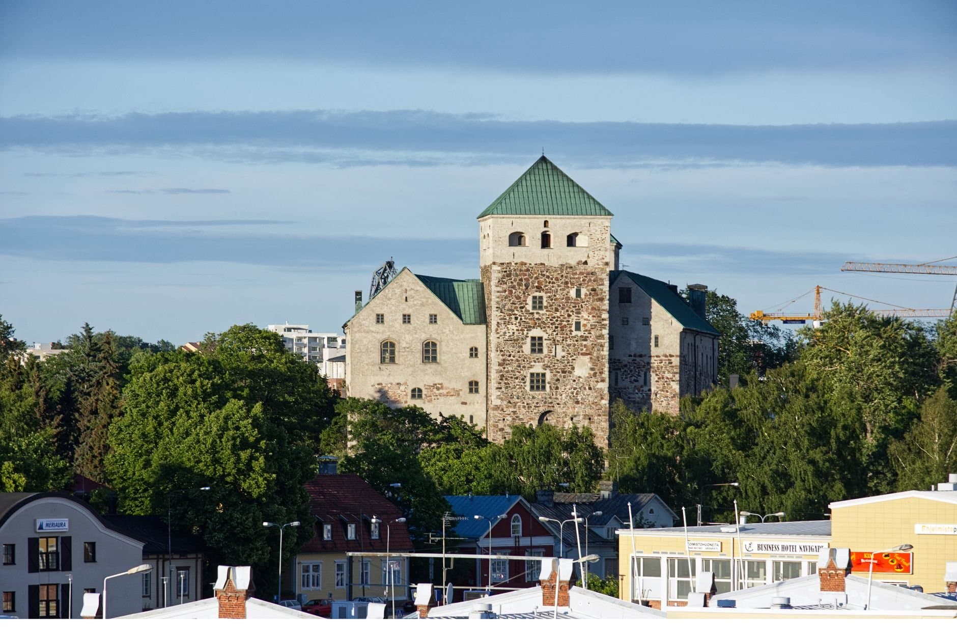 Turku Castle surrounded by lush greenery and modern architecture in summer.