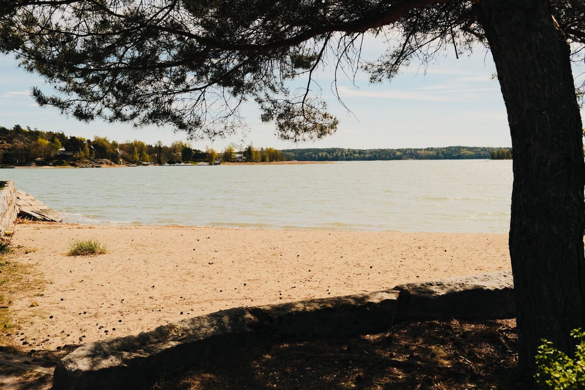 A serene beach in Turku, Finland with calm waters and lush trees under a sunny sky.