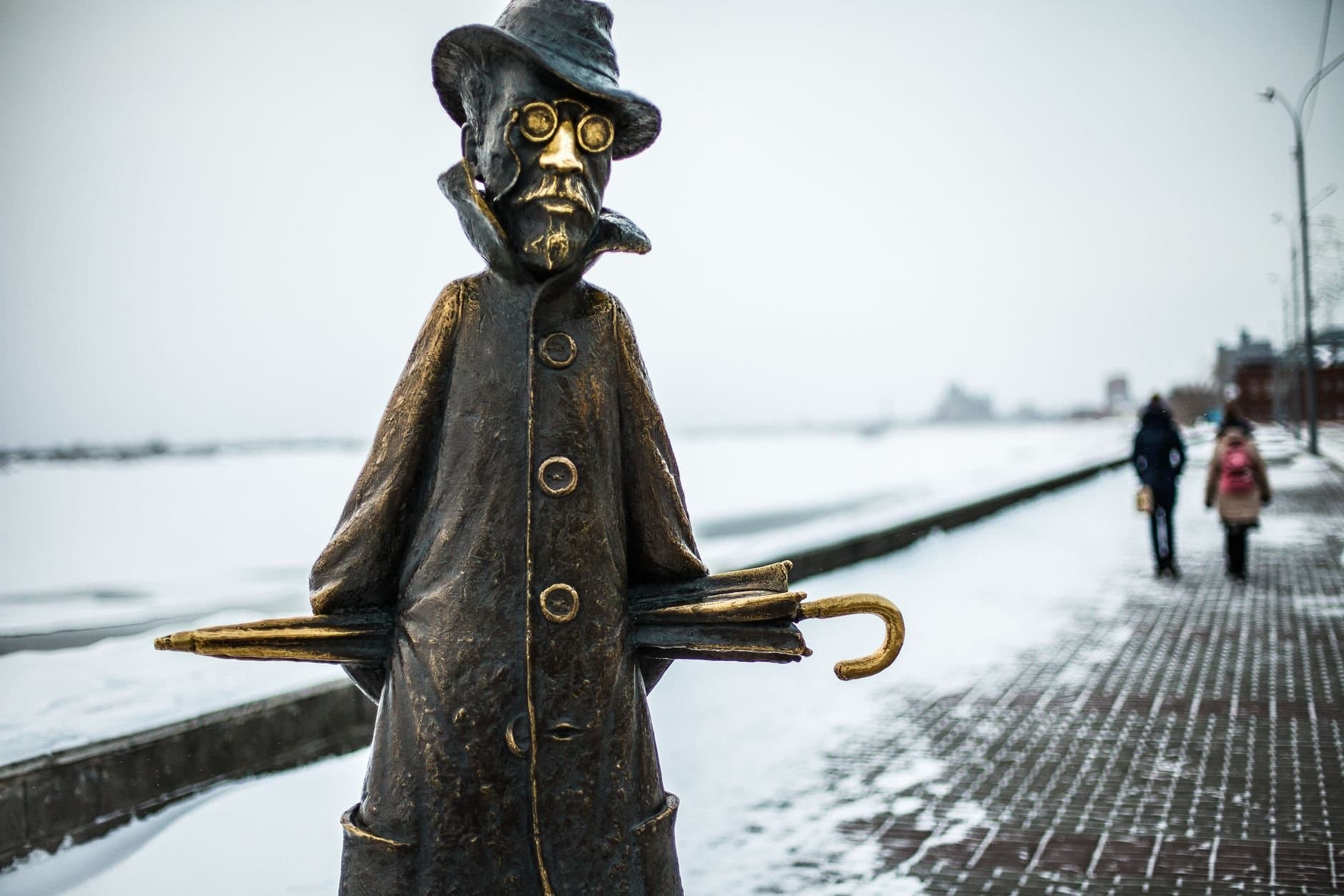 Bronze statue with umbrella in a winter scene on Tomsk's snow-covered embankment, Russia.