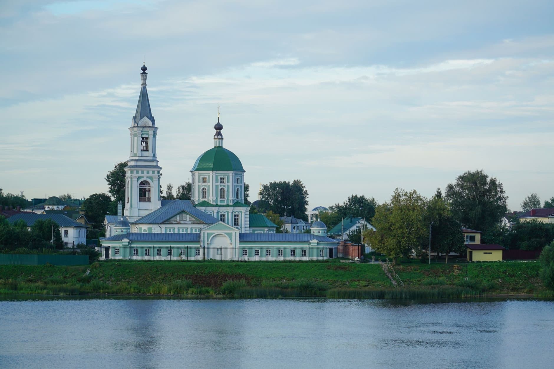 Scenic view of an Orthodox church with green domes by the river in Tver, Russia, capturing architectural elegance.