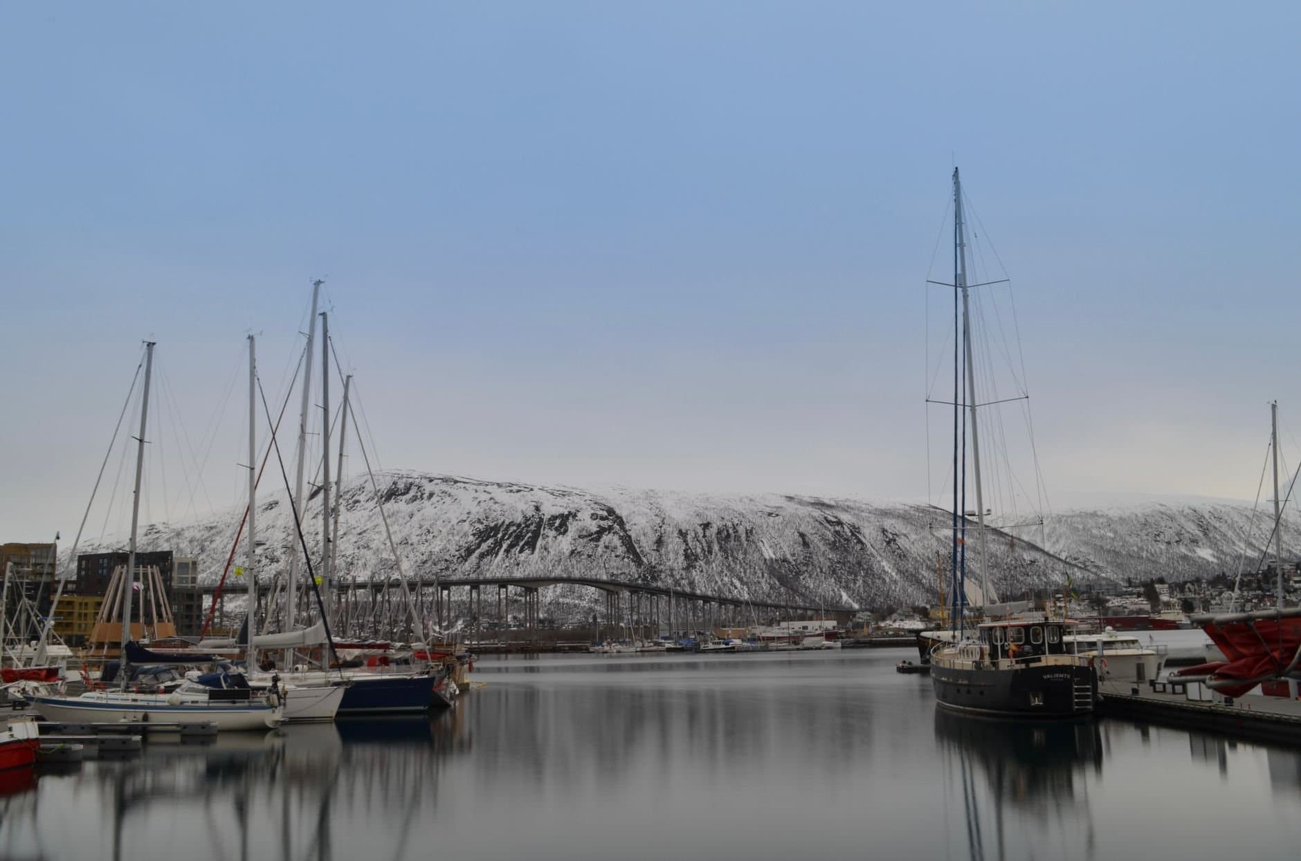 A scenic winter view of Tromsø harbor with boats and snowy mountains in Troms, Norway.