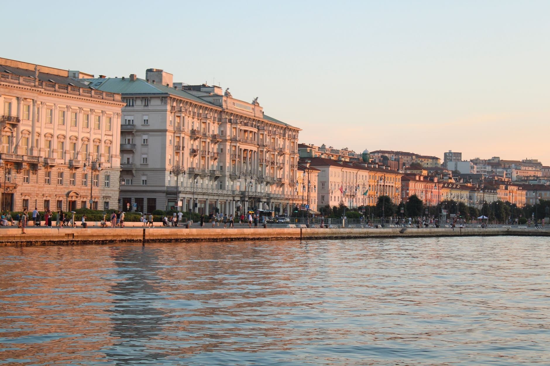 Beautiful sunset over historic waterfront buildings in Trieste, Italy reflecting off the Adriatic Sea.