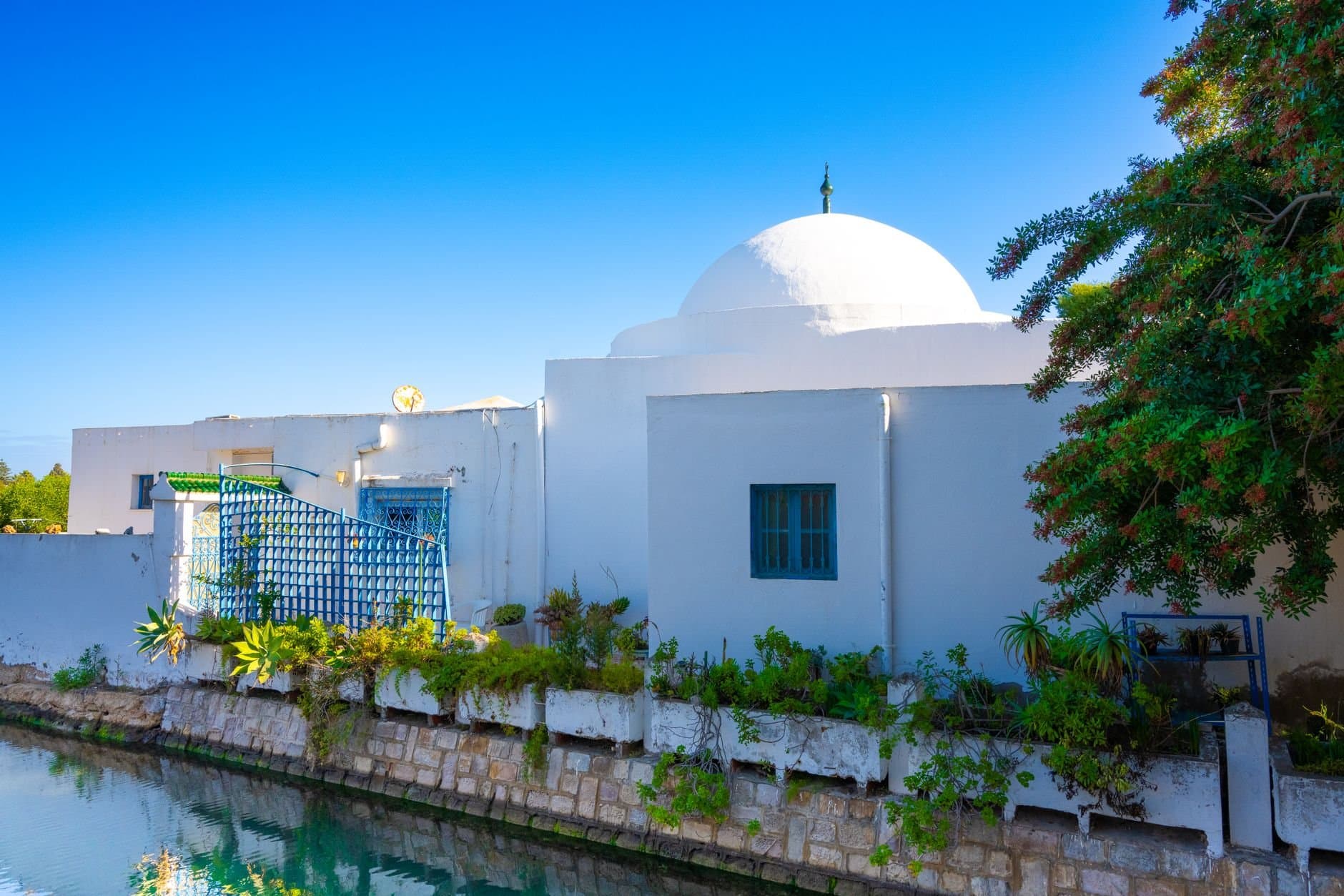 Beautiful dome-roofed building in Tunisia reflected on tranquil water under a clear blue sky.