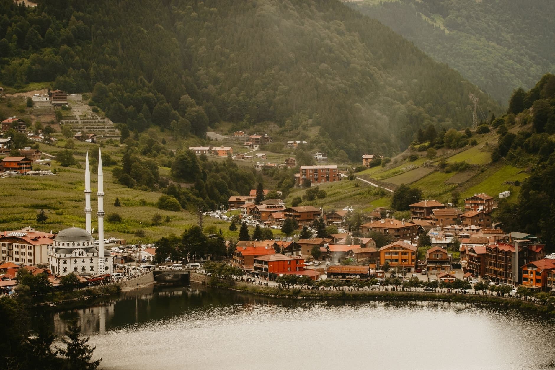 Scenic view of Uzungöl valley featuring a mosque, lush hills, and a tranquil lake in Turkey.