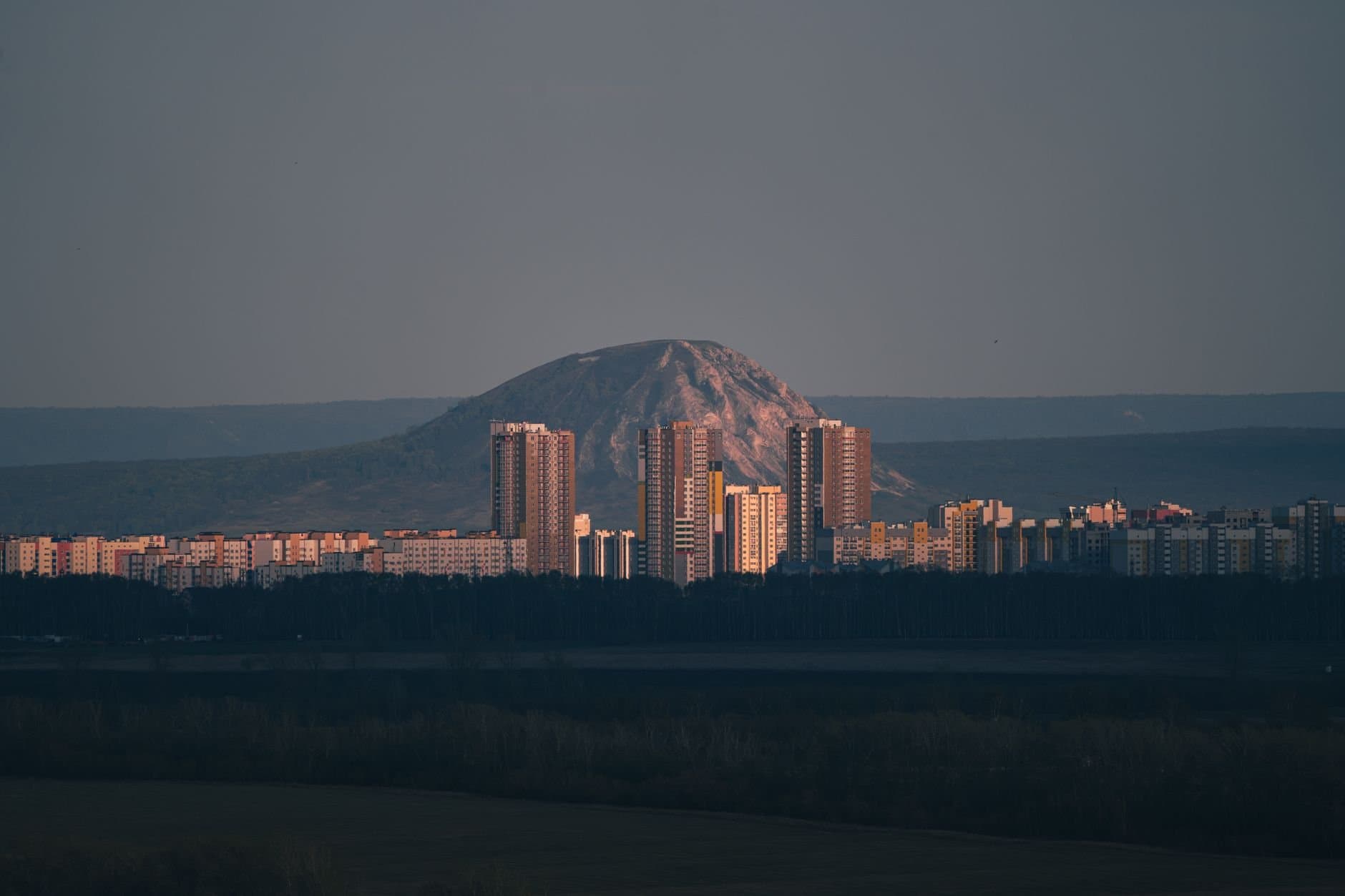 A stunning cityscape of Ufa at dusk showcasing high-rise buildings and a mountain backdrop.