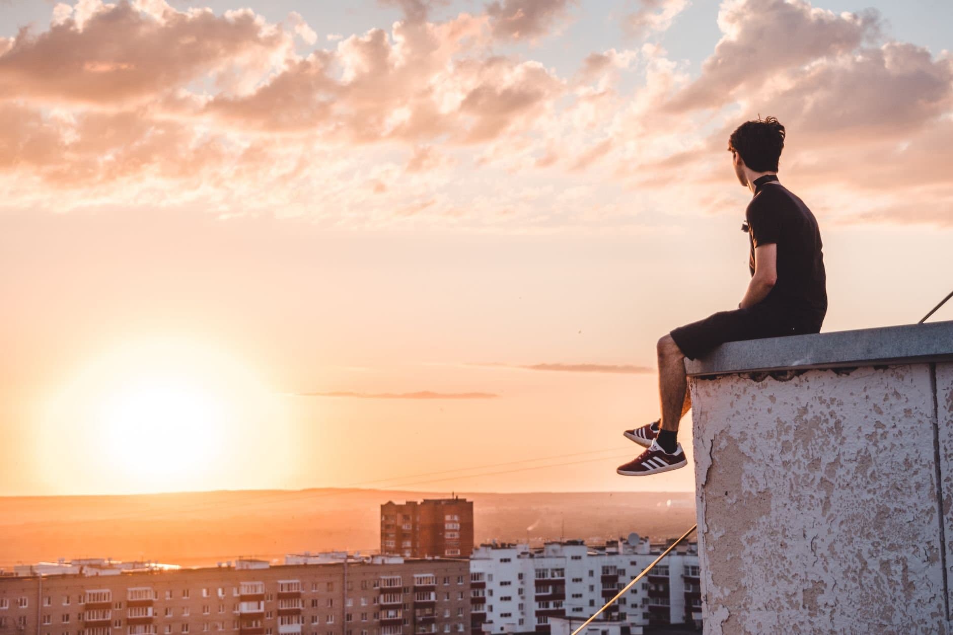 A young man sitting on a rooftop in Ufa, Russia, watching a vibrant sunset.