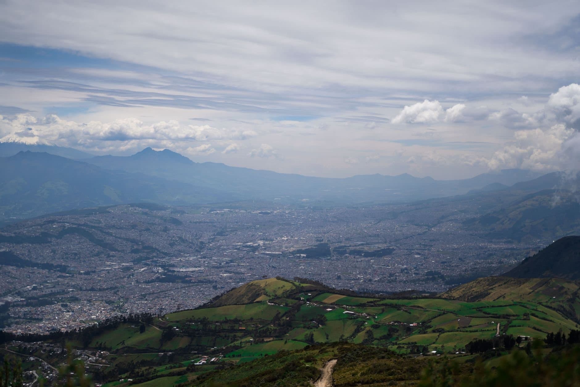 A breathtaking aerial shot of Quito, displaying lush valleys and rugged mountains under a dynamic sky.