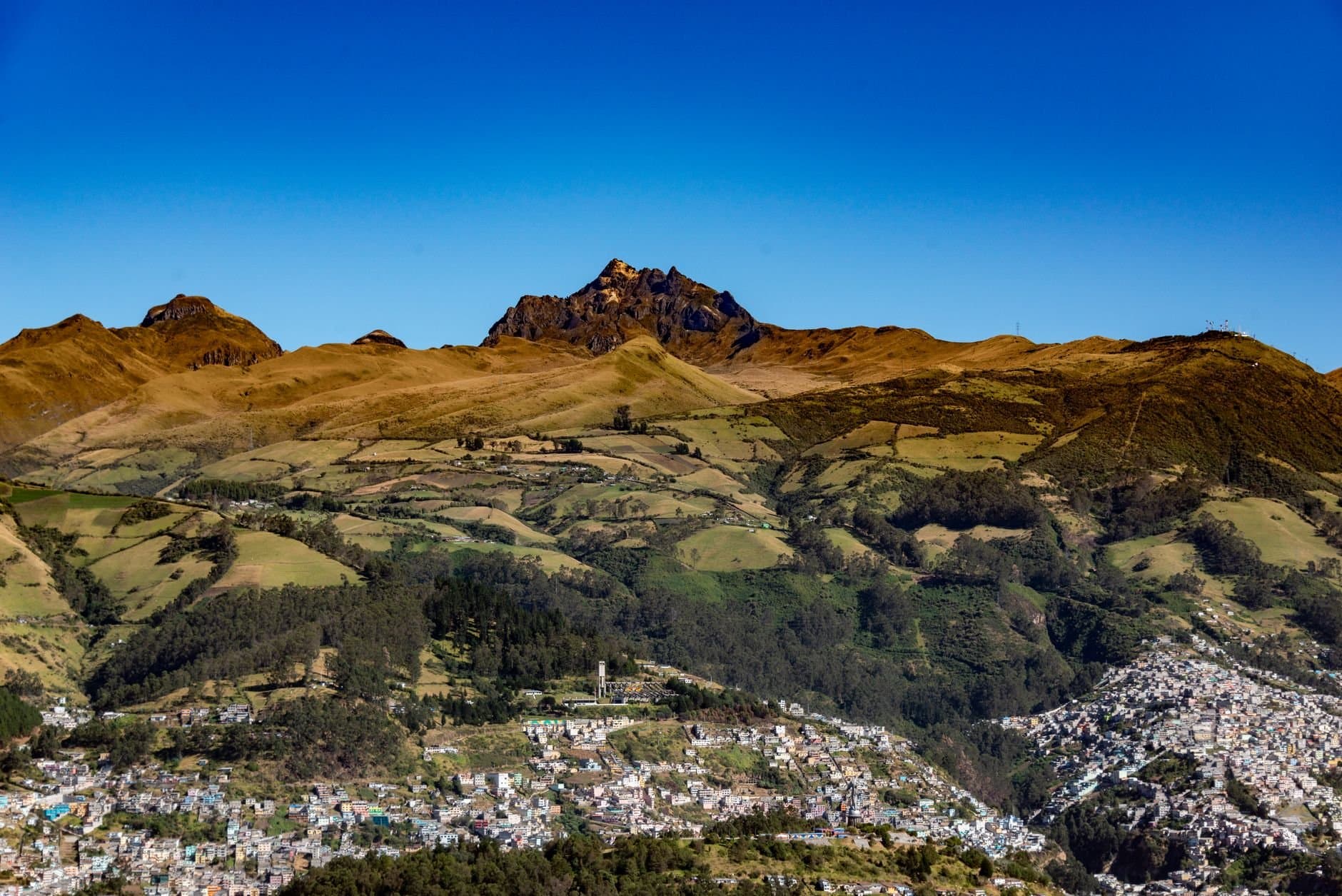 Stunning aerial view of Pichincha Volcano surrounded by green hills and urban outskirts of Quito, Ecuador.