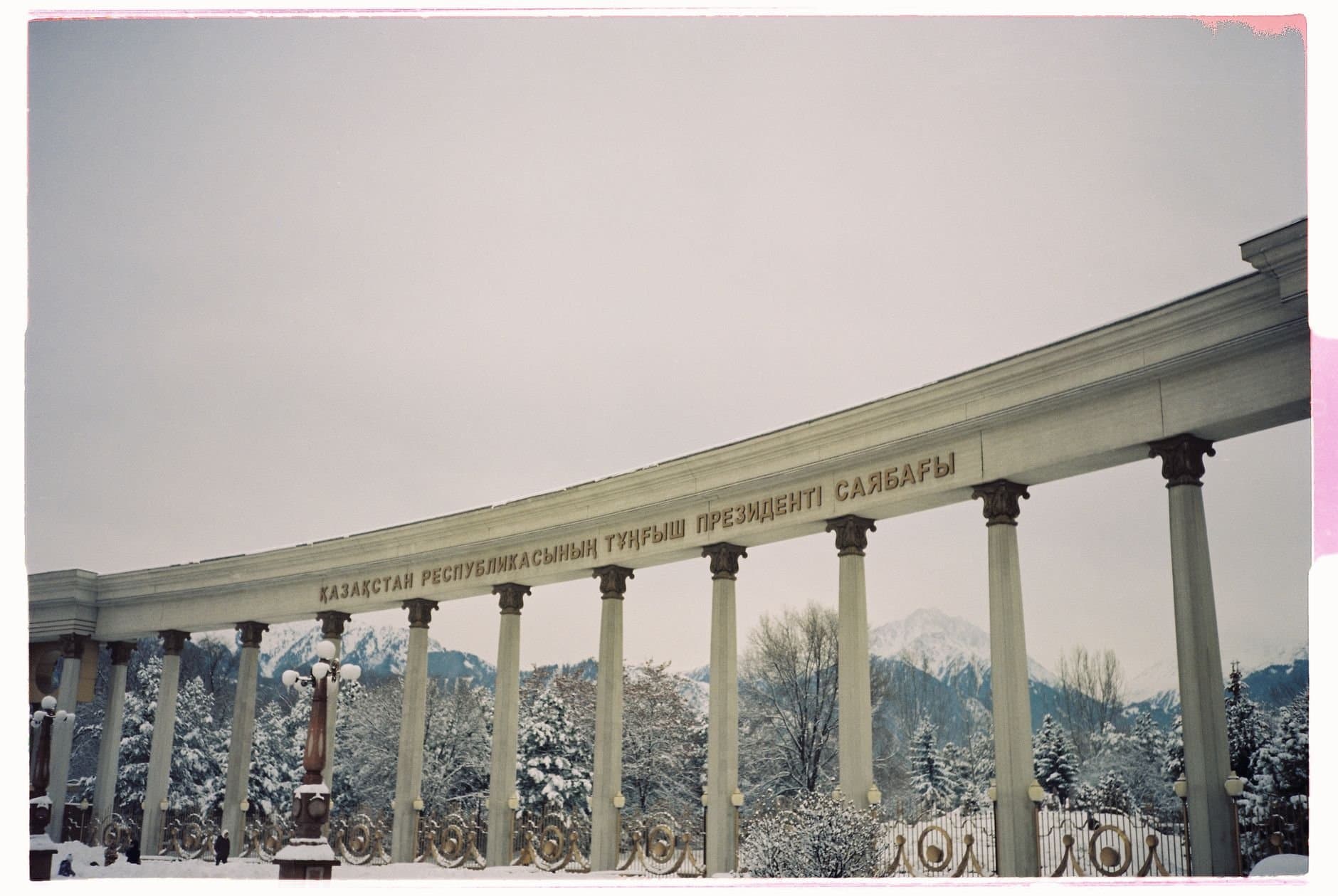 Snow-covered neoclassical colonnade with Cyrillic script in Almaty, Kazakhstan.