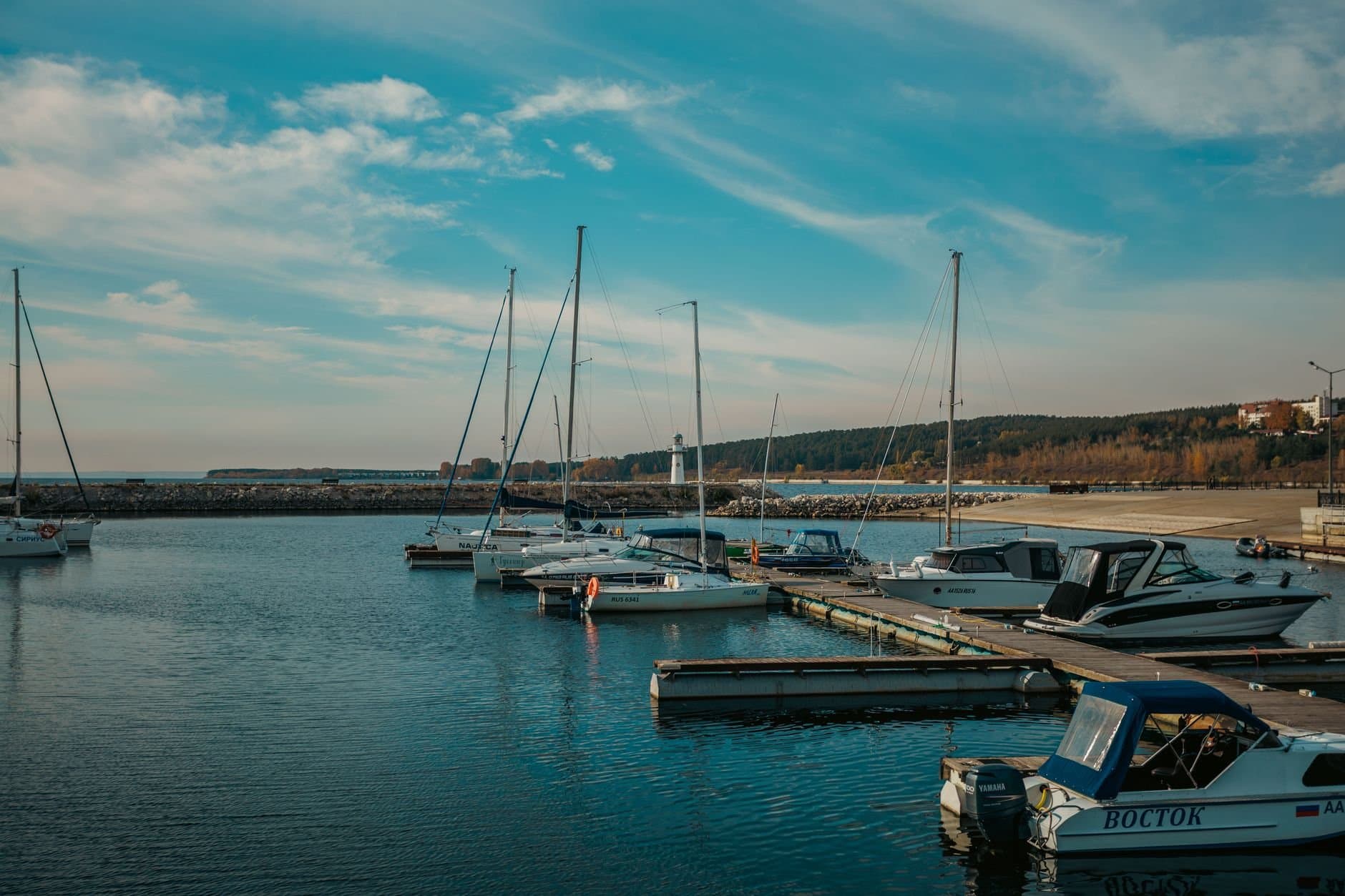 Scenic view of a marina with sailboats and a lighthouse under a clear blue sky, perfect for travel enthusiasts.