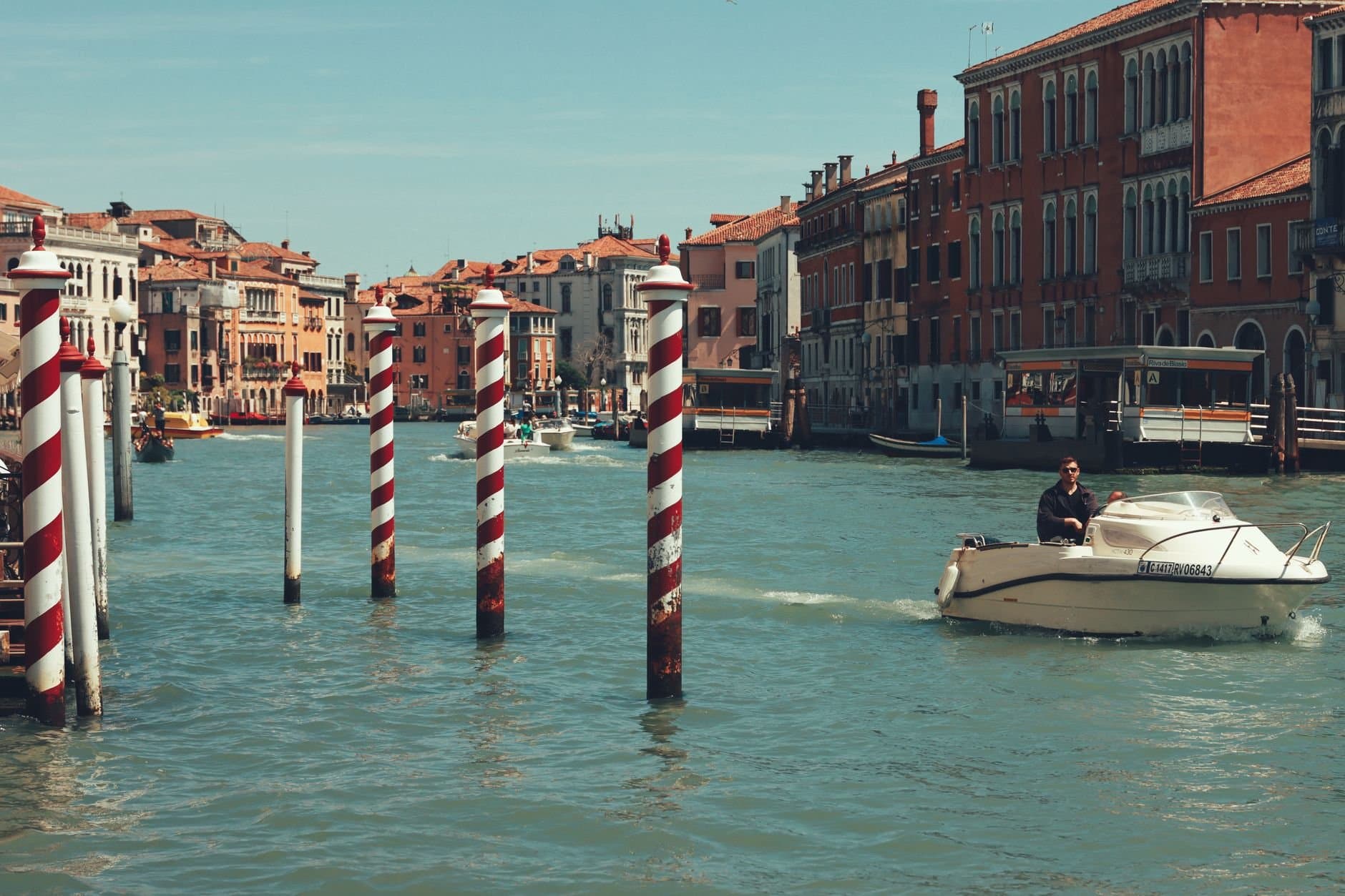 A serene view of a motorboat cruising past iconic striped poles on Venice's Grand Canal.