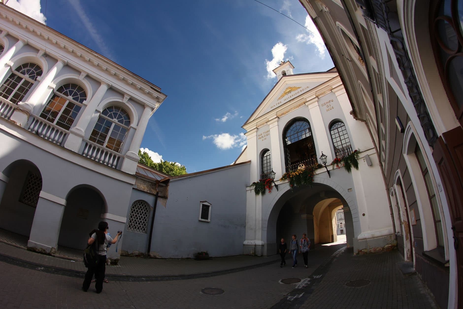 Tourists exploring the historic Gates of Dawn in Vilnius, Lithuania on a sunny day.