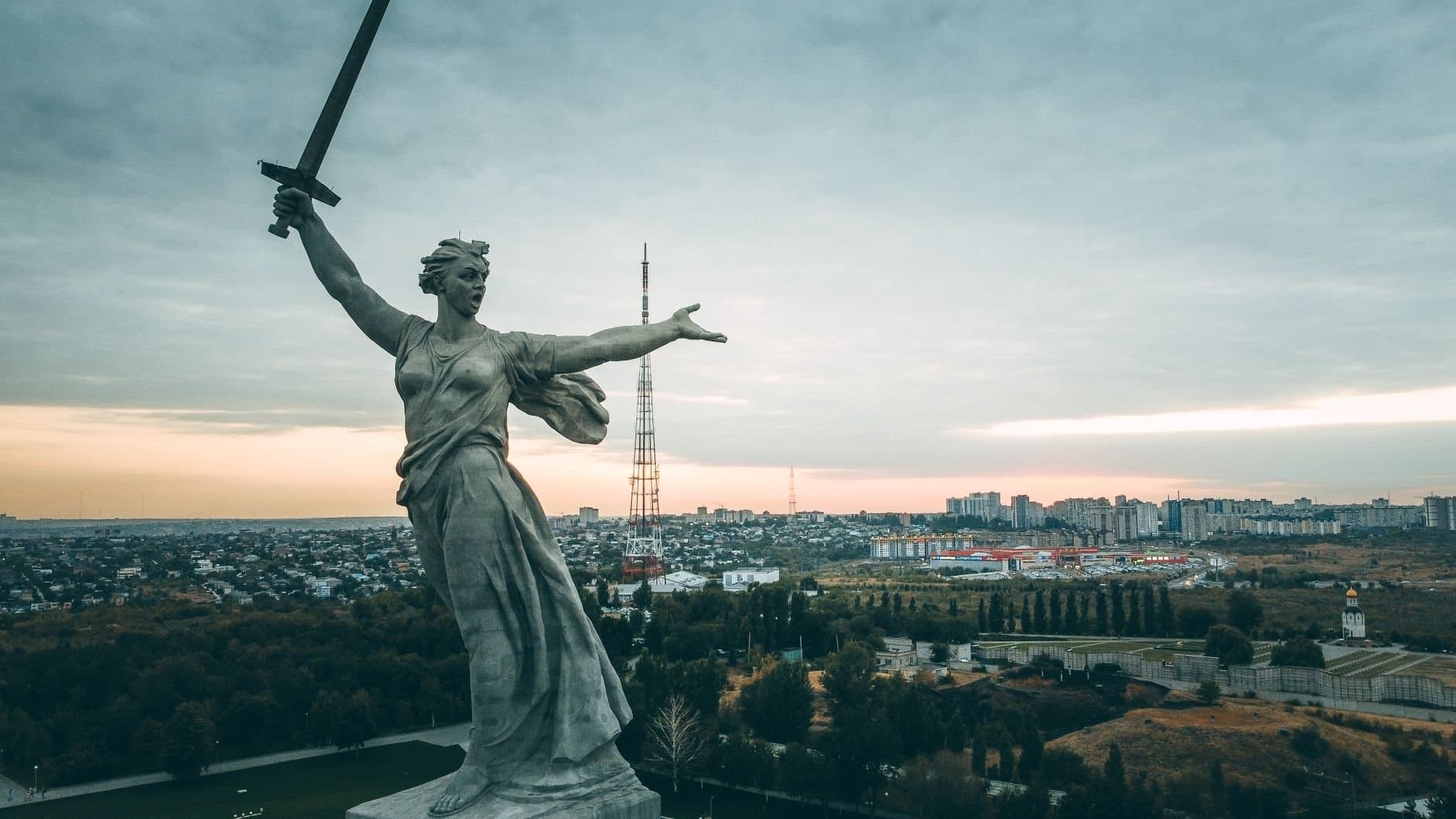 Dramatic aerial view of The Motherland Calls statue in Volgograd at sunrise, overlooking the cityscape.