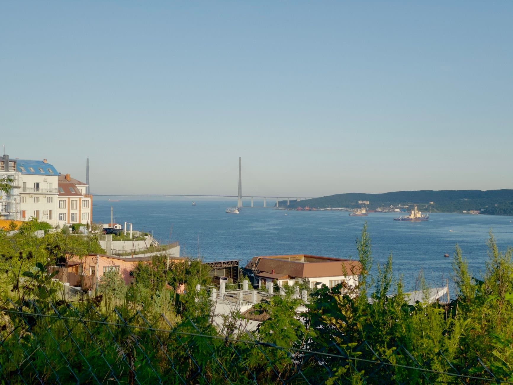 Panoramic view of urban landscape with Russky Bridge and serene water on a clear day.