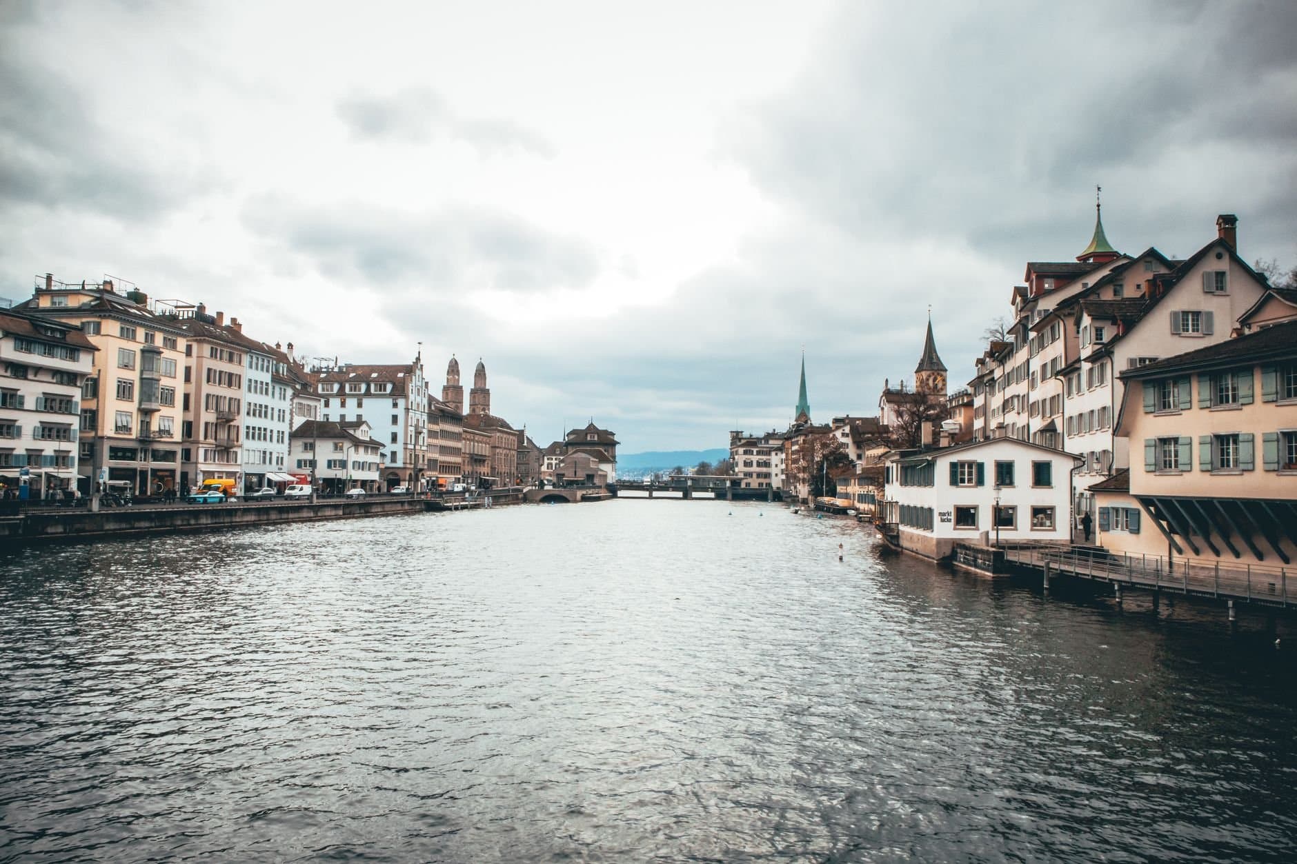 Scenic view of Zurich's historic buildings along the Limmat River under a cloudy sky.