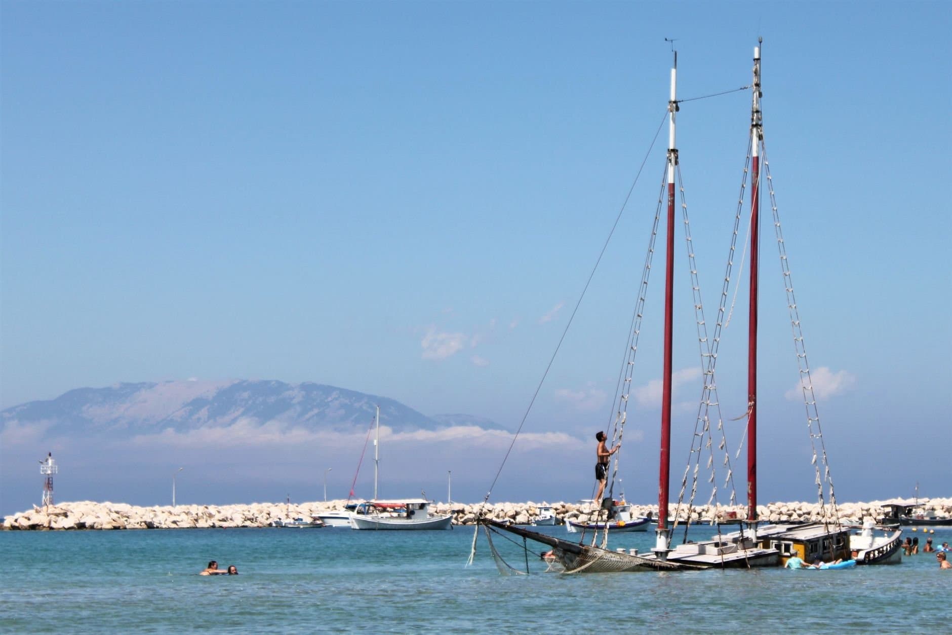 Enjoy a sunny day at Zakinthos harbor with sailboats and swimmers.