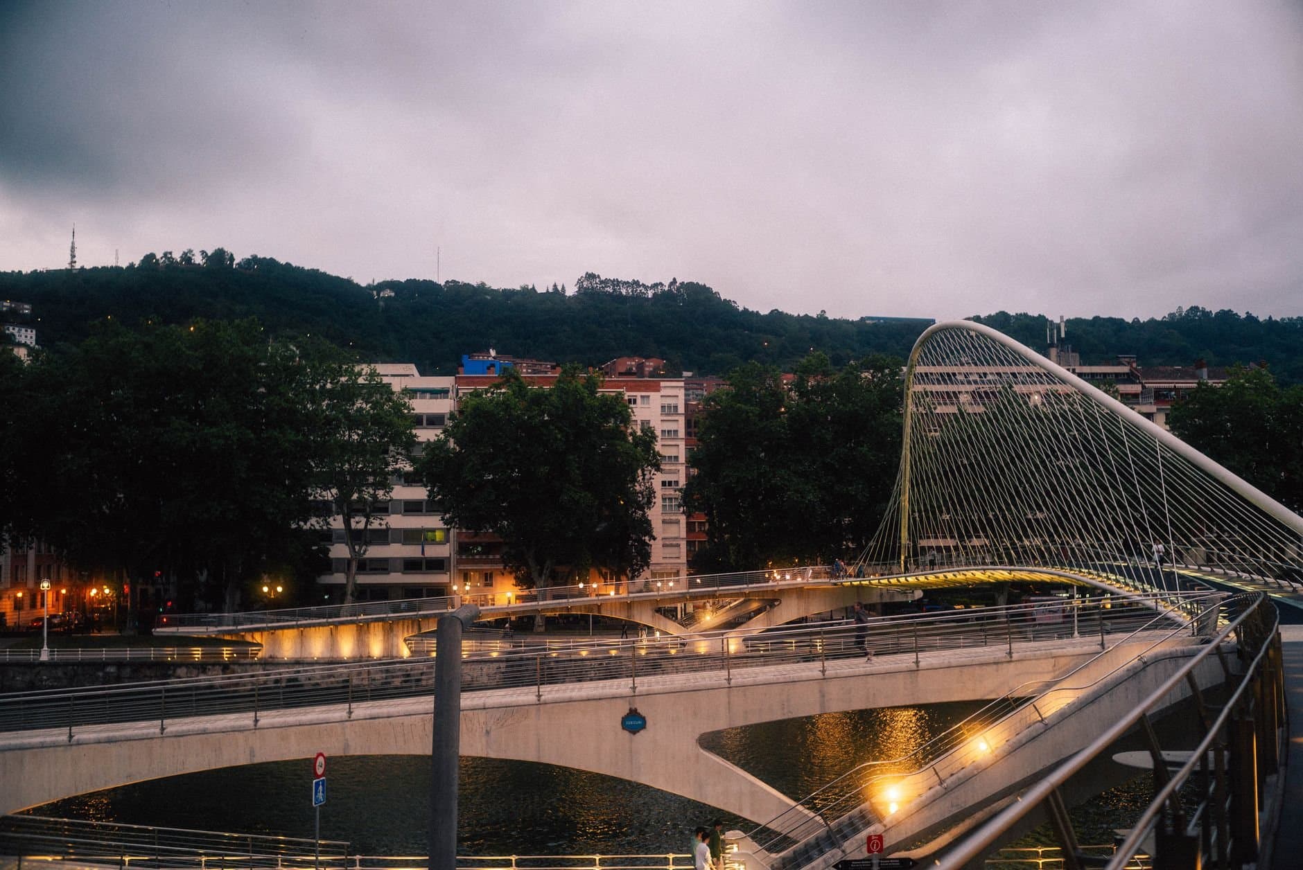 A modern architectural marvel, the Zubizuri Bridge in Bilbao lit up at dusk.
