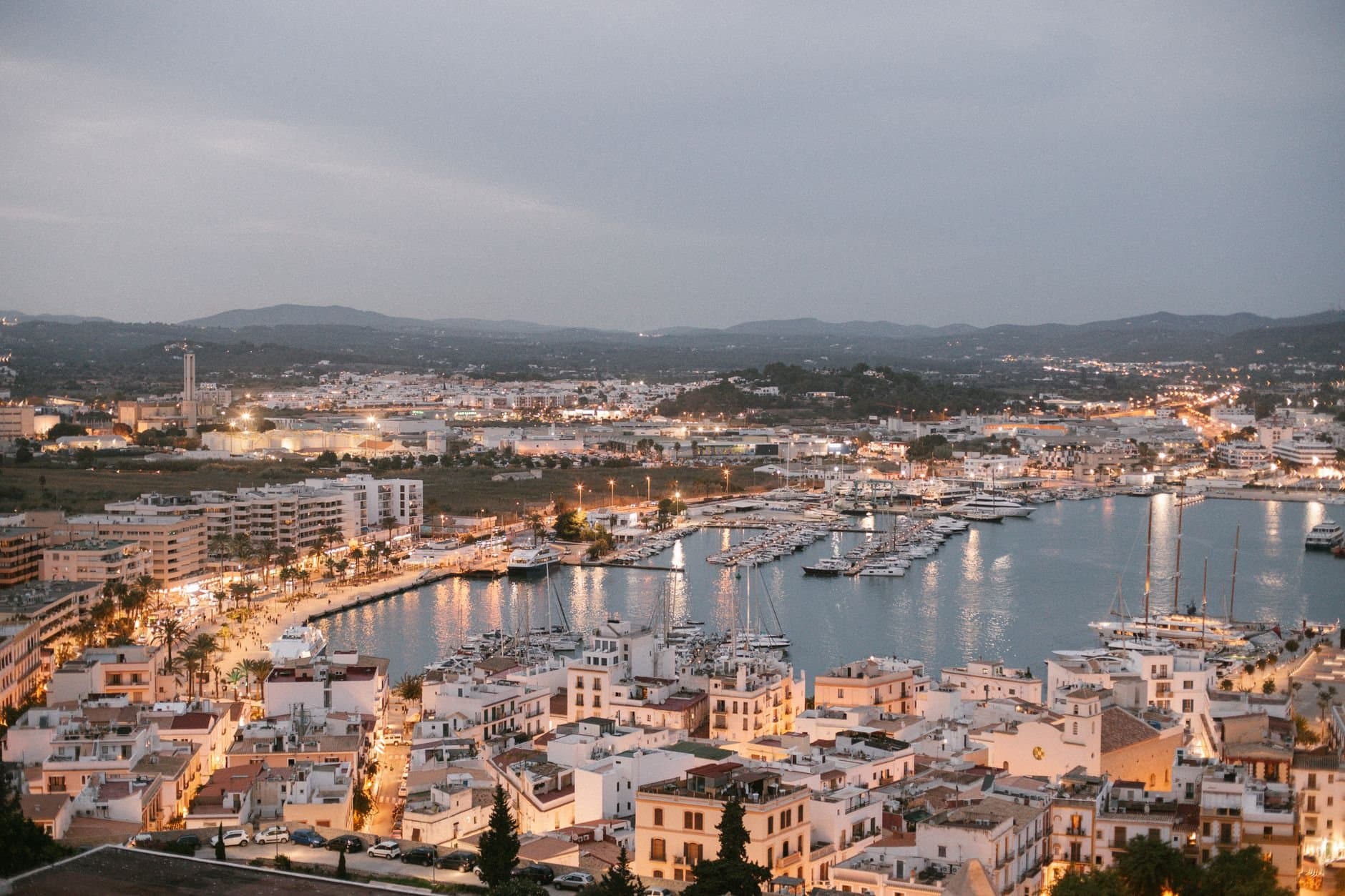 A scenic aerial view of Ibiza's marina at dusk, showcasing vibrant city lights and bustling harbor in Spain.