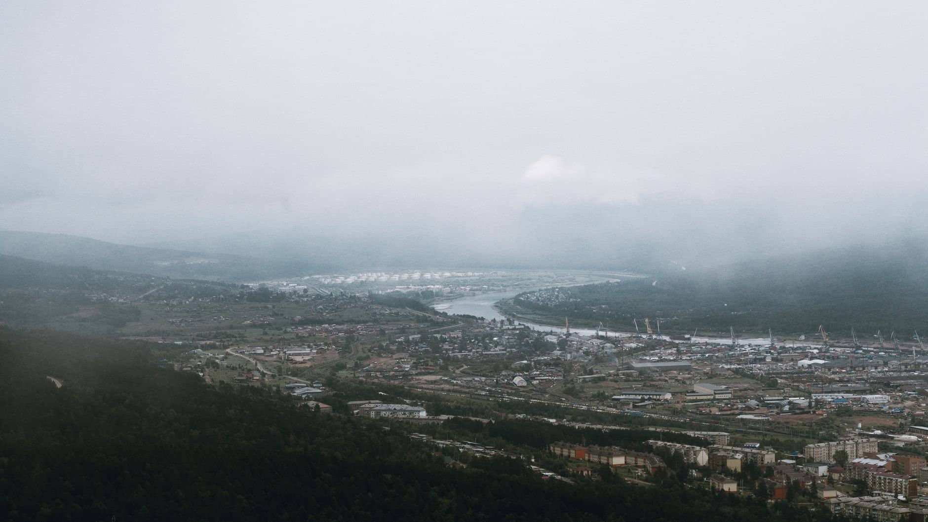 Scenic aerial view of Ust-Kut with fog, river, and mountains in a winter landscape.