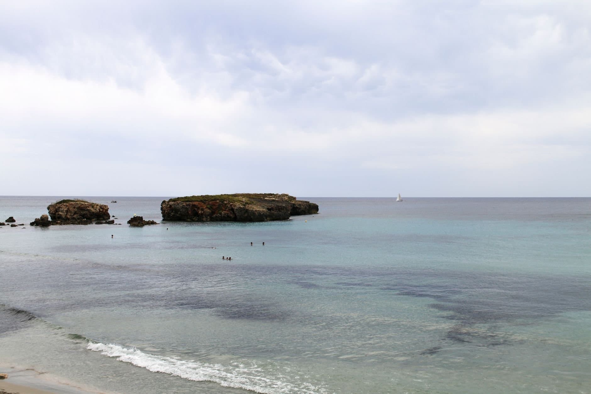 Serene view of the Mediterranean Sea near Ciutadella de Menorca with scattered islets and a distant sailboat.