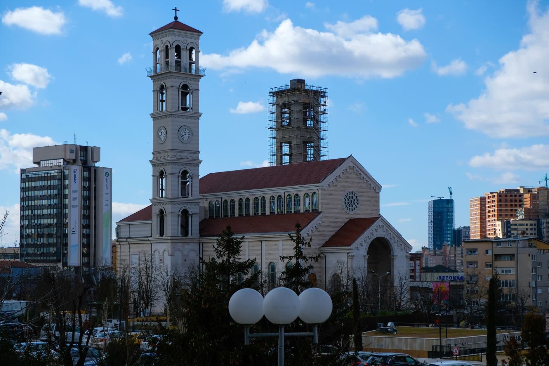 Catholic Cathedral surrounded by modern cityscape in Pristina, an architectural landmark blending past and present.