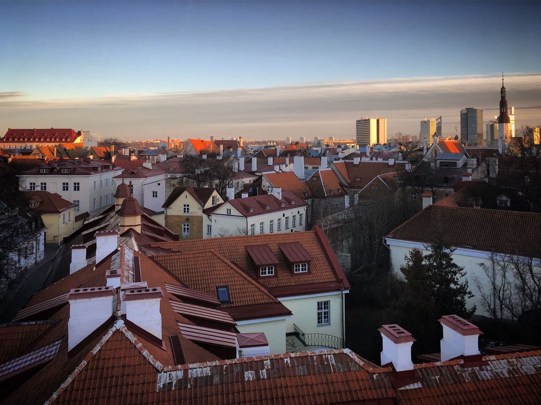 Stunning aerial view of Tallinn's Old Town with red rooftops and modern skyline at sunset.